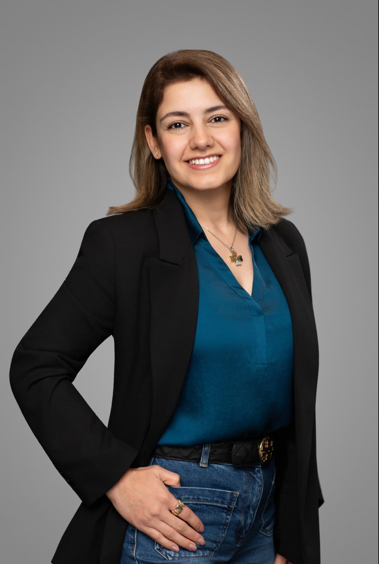 Bita Samiei smiling, wearing a black blazer over a teal blouse, against a soft grey background